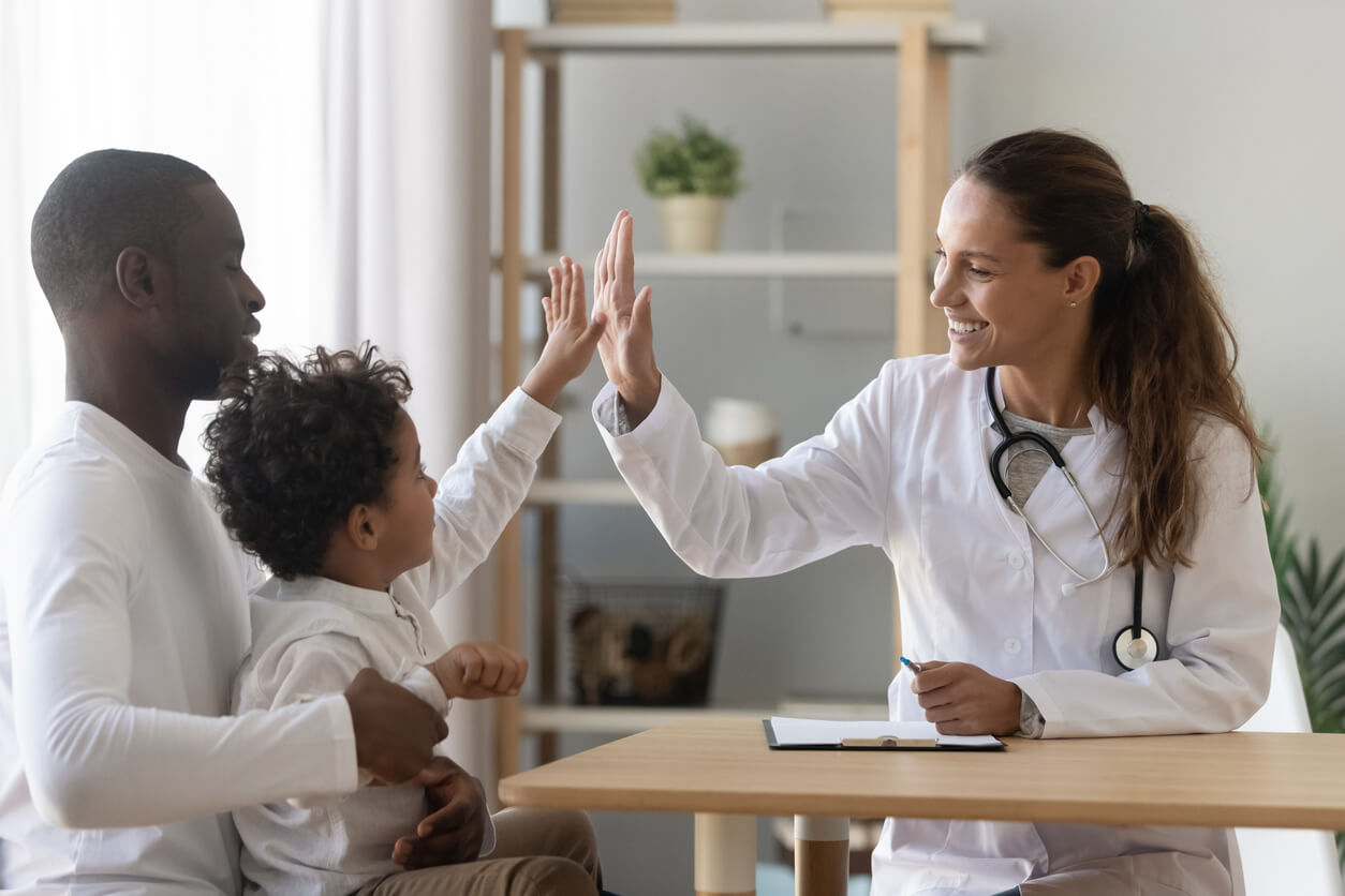 Family medicine doctor giving a high-five to a child, who is sitting in his father's lap.