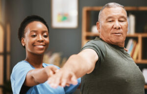 A Black female physiotherapist is assisting a patient with arthritis in stretching and improving muscle mobility during physical therapy.