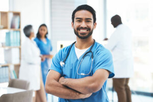 A smiling and happy primary care doctor stands with arms crossed.