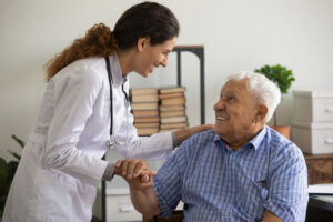 A grateful elderly man, who is unwell, is holding the hand of a nurse to express his appreciation for her help.