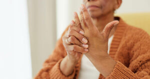 An elderly woman in a nursing home is struggling with hand pain and arthritis due to a medical injury.