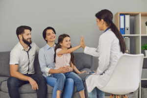 A smiling girl is giving a high five to a woman family medicine doctor during a medical consultation in the clinic.