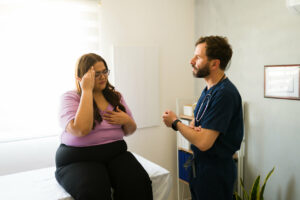 female patient communicating health concerns while seated on exam table during medical consultation with family doctor