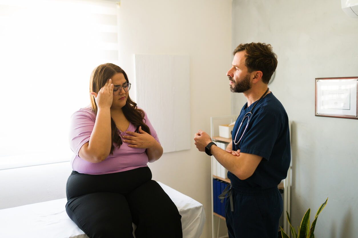 female patient communicating health concerns while seated on exam table during medical consultation with family doctor