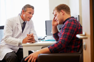 Primary Care Doctor Treating Male Patient Suffering With Depression And Mental Health Issues.